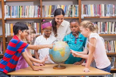 Cute pupils and teacher looking at globe in library