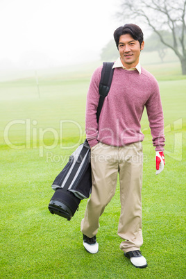 Golfer standing holding his golf bag smiling at camera
