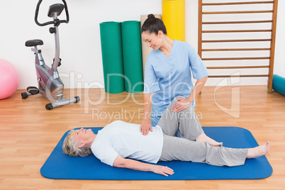 Therapist working with senior woman on exercise mat