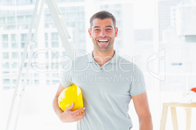 Cheerful handyman holding hardhat at construction site