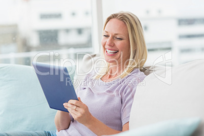 Cheerful woman using tablet computer on sofa