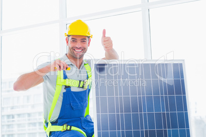 Male worker tightening solar panel while gesturing thumbs up