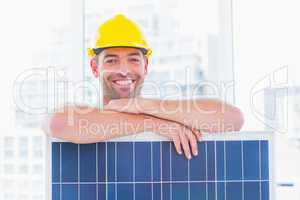 Smiling manual worker with solar panel in office