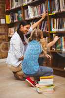 Teacher and little girl selecting book in library