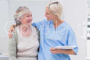 Happy nurse with arm around senior patient in clinic