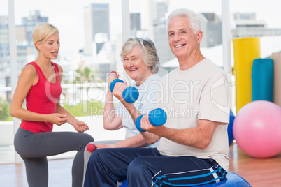 happy senior couple lifting dumbbells while instructor guiding t