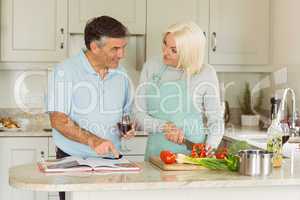 Happy mature couple having red wine while making dinner