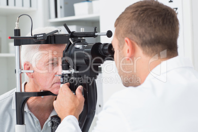 Optician examining senior patients eyes through slit lamp