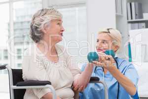 Nurse looking at patient while assisting her in lifting dumbbell