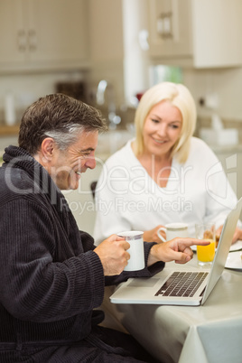 Mature couple having breakfast together man using laptop