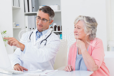 Doctor showing reports to senior patient on computer