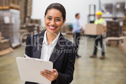 Smiling warehouse manager writing on clipboard