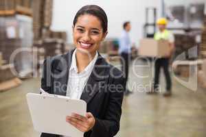 Smiling warehouse manager writing on clipboard