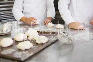 Colleagues kneading uncooked dough on worktop