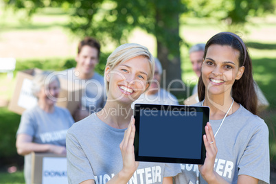 Happy volunteer friends showing tablet pc screen