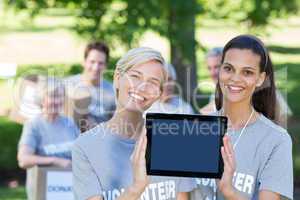 Happy volunteer friends showing tablet pc screen