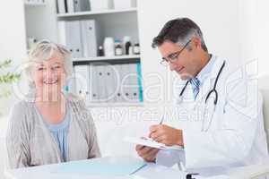 Doctor writing prescription while female patient smiling