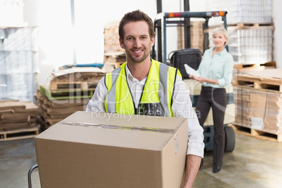 Smiling warehouse worker carrying box