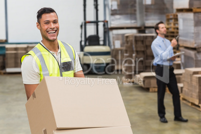 Smiling warehouse worker moving boxes on trolley