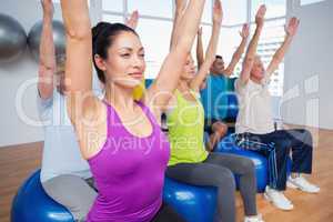 People sitting on exercise balls with hands raised
