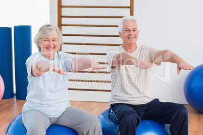 Senior couple with arms raised sitting on exercise ball
