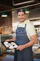 Smiling worker in apron holding tray of meringue