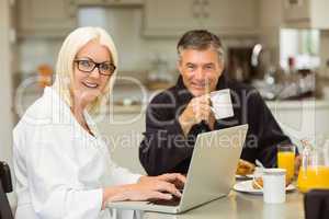 Mature couple having breakfast together woman using laptop