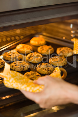 Woman taking tray of fresh cookies out of oven