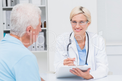 Female doctor writing prescription for senior man