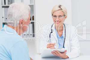 Female doctor writing prescription for senior man