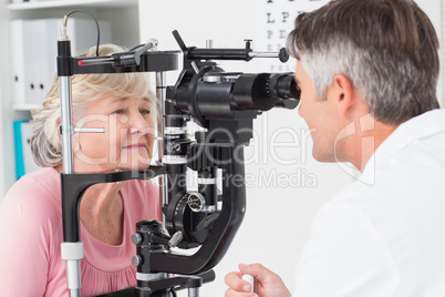 Optician examining senior female patient through slit lamp