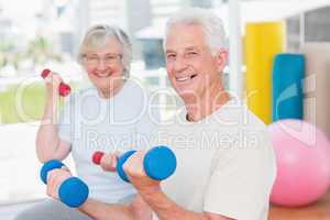 Happy senior couple lifting dumbbells in gym