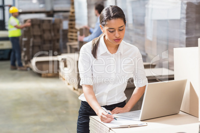 Warehouse manager using laptop and clipboard