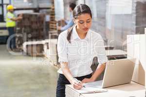 Warehouse manager using laptop and clipboard