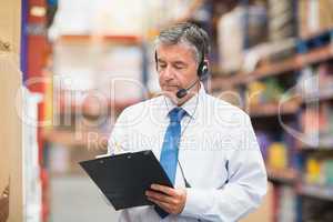 Warehouse manager wearing headset writing on clipboard