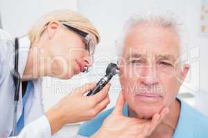 Doctor examining senior patients ear with otoscope
