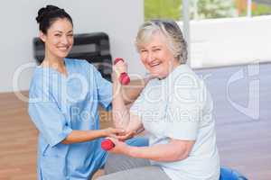 Instructor assisting senior woman in lifting dumbbells