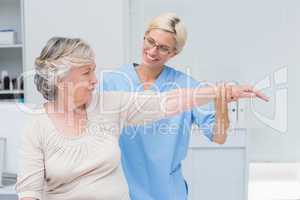 Nurse assisting senior patient in exercising at clinic