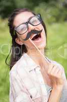 Pretty brunette smiling at camera with fake mustache