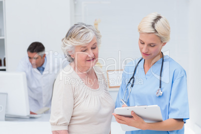 Nurse communicating with patient while doctor using computer