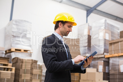 Warehouse manager wearing hard hat using tablet