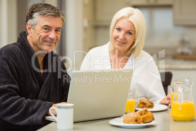 Mature couple having breakfast together man using laptop