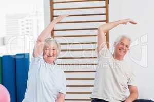 Senior couple doing stretching exercise in fitness studio