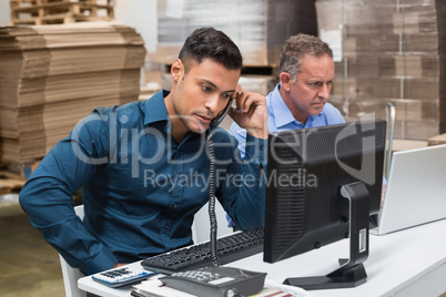 Warehouse managers using telephone and laptop