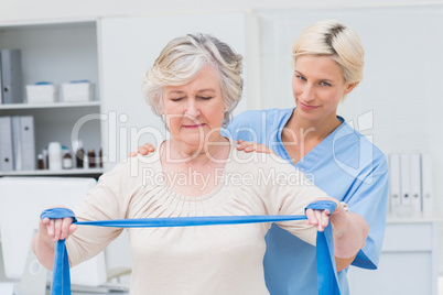 Nurse assisting senior woman in exercising with resistance band