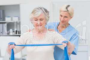 Nurse assisting senior woman in exercising with resistance band