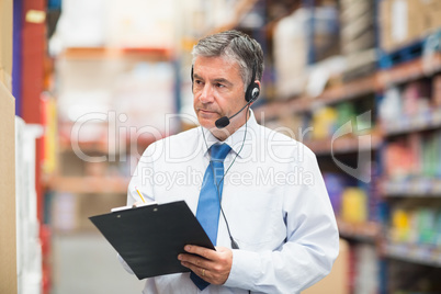 Warehouse manager wearing headset writing on clipboard