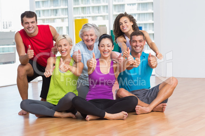 Fit men and women gesturing thumbs up in fitness studio