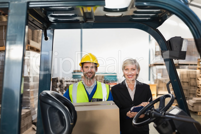 Warehouse manager smiling at camera with forklift driver