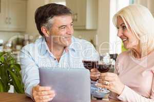 Happy mature couple using tablet drinking red wine